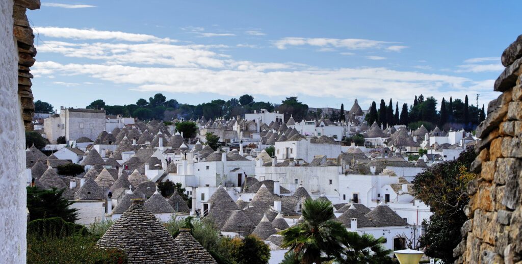 A picturesque view of iconic trulli houses in Alberobello, Italy, under a bright sky.